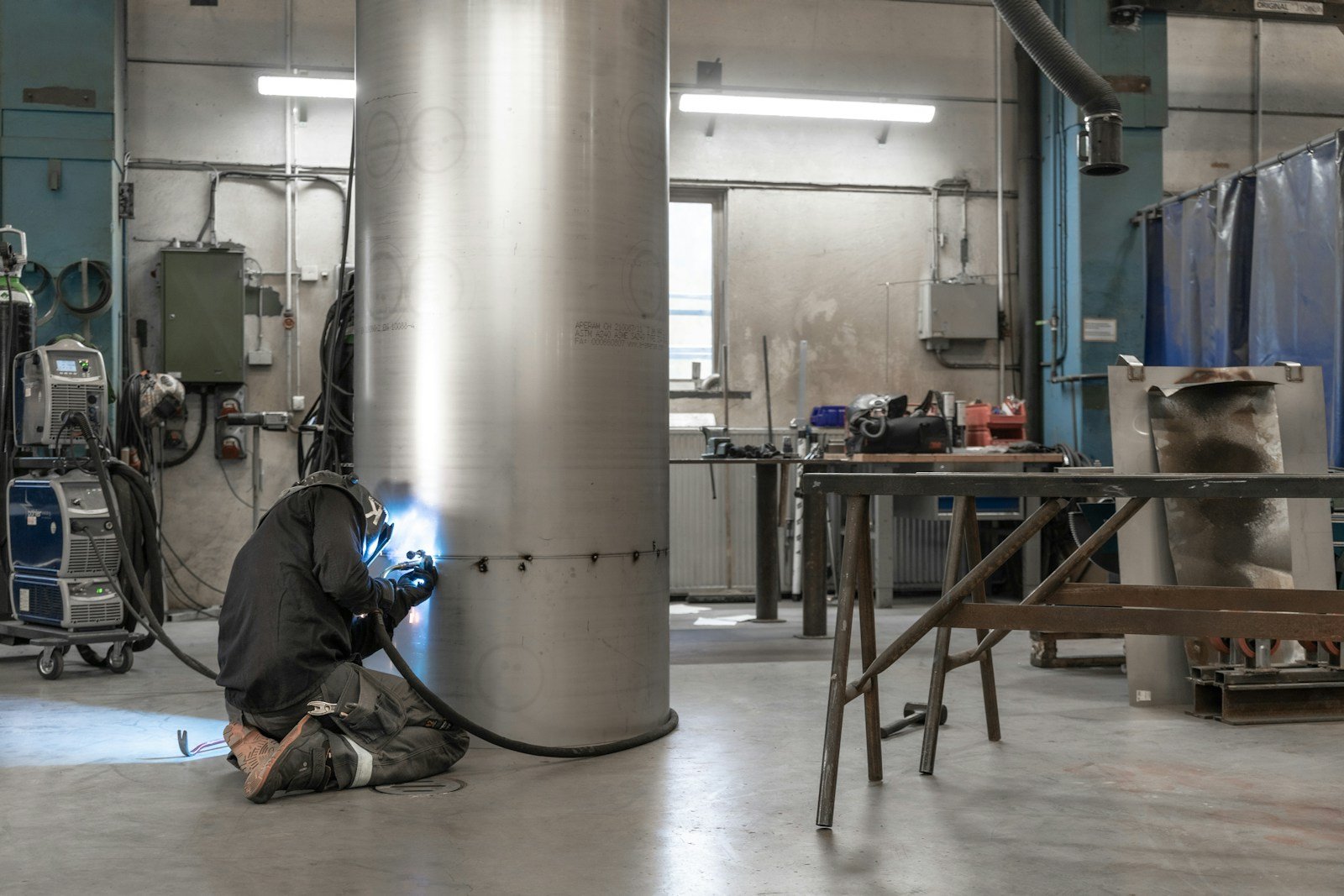 A welder in protective equipment joins an industrial metal cylinder.